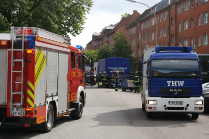 KI-generiertes Symbolbild: Symbolbild: Straßenszene mit Feuerwehrfahrzeug, THW-Lkw und Einsatzkräften