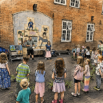 KI-generiertes Symbolbild: Symbolbild: Szene einer Kita-Abschlussveranstaltung mit Kindern und Erwachsenen in einem Innenhof