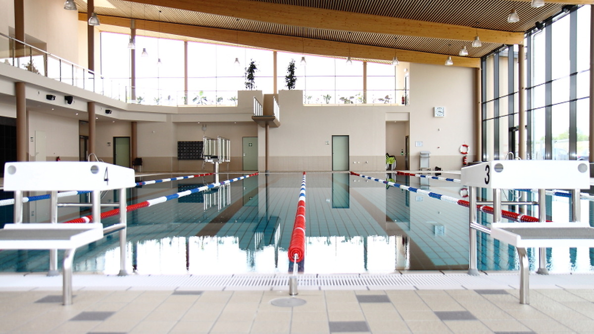 Leeres Hallenbad mit gefülltem Schwimmbecken, Startblöcken und abgetrennten Bahnen